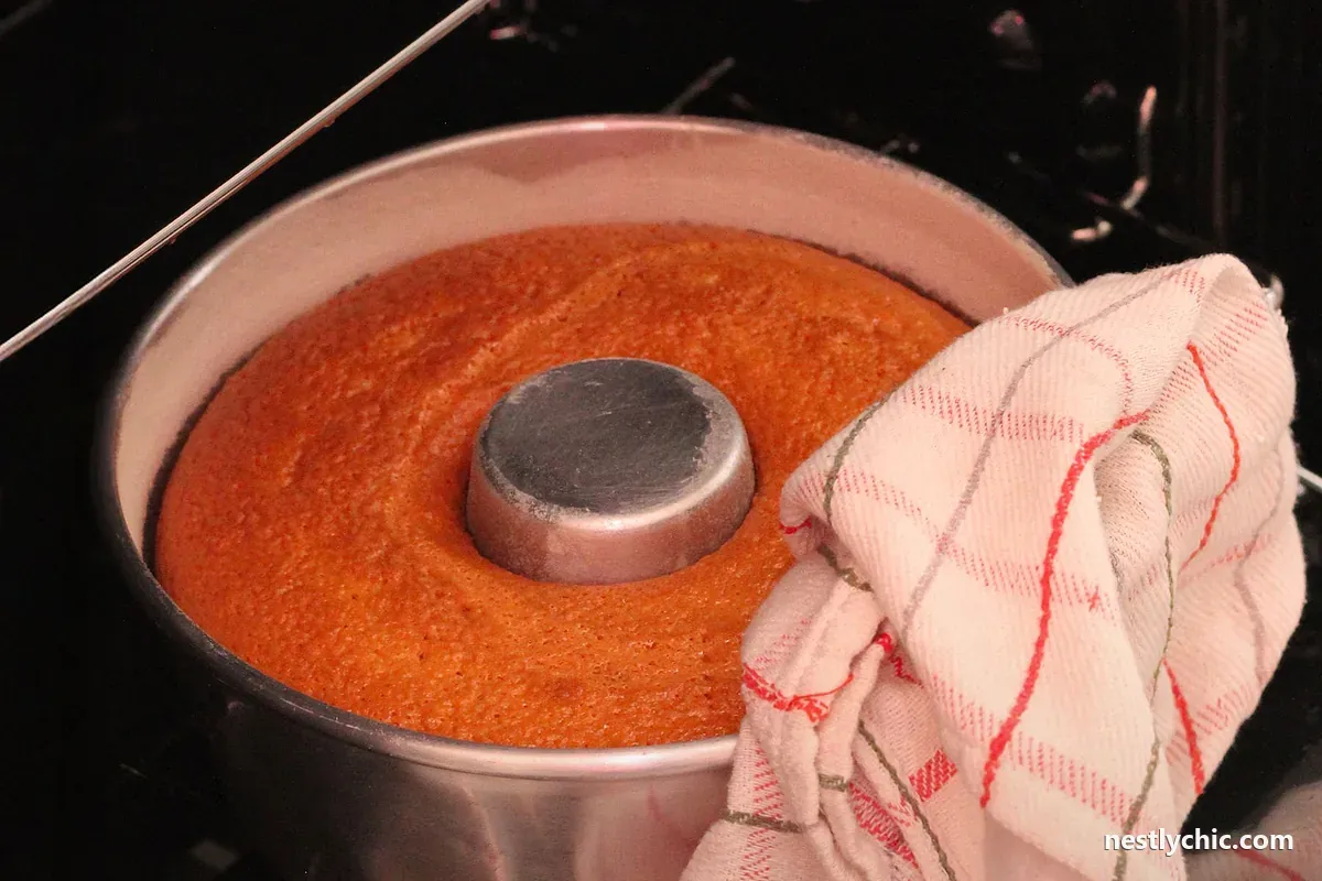 An orange cake cooling in a metal pan in the oven